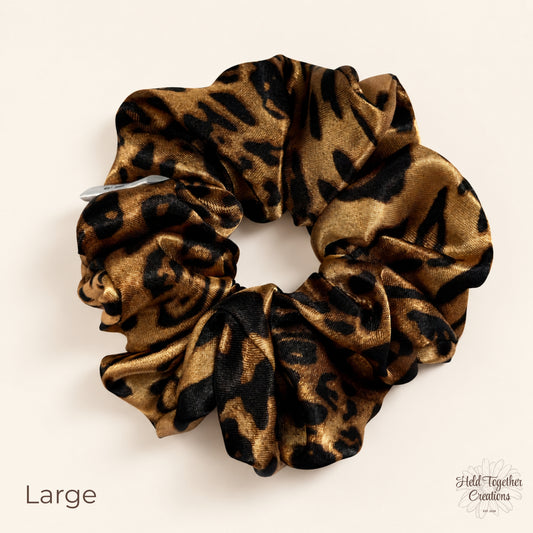 Large leopard satin scrunchie with golden brown and black animal print on a soft neutral background.