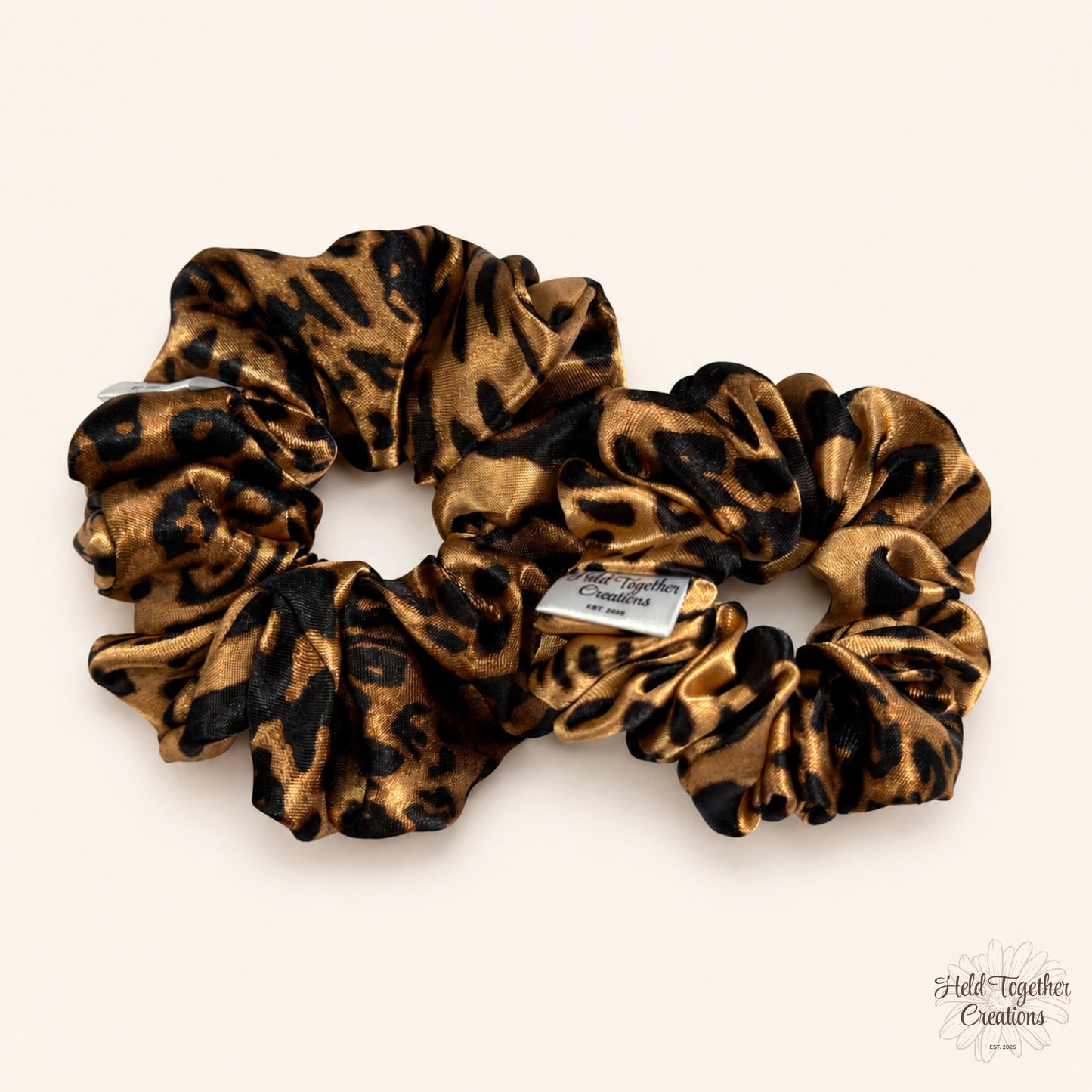 Small and large leopard satin scrunchies displayed side by side on a neutral background.