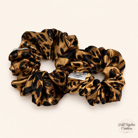 Small and large leopard satin scrunchies displayed side by side on a neutral background.