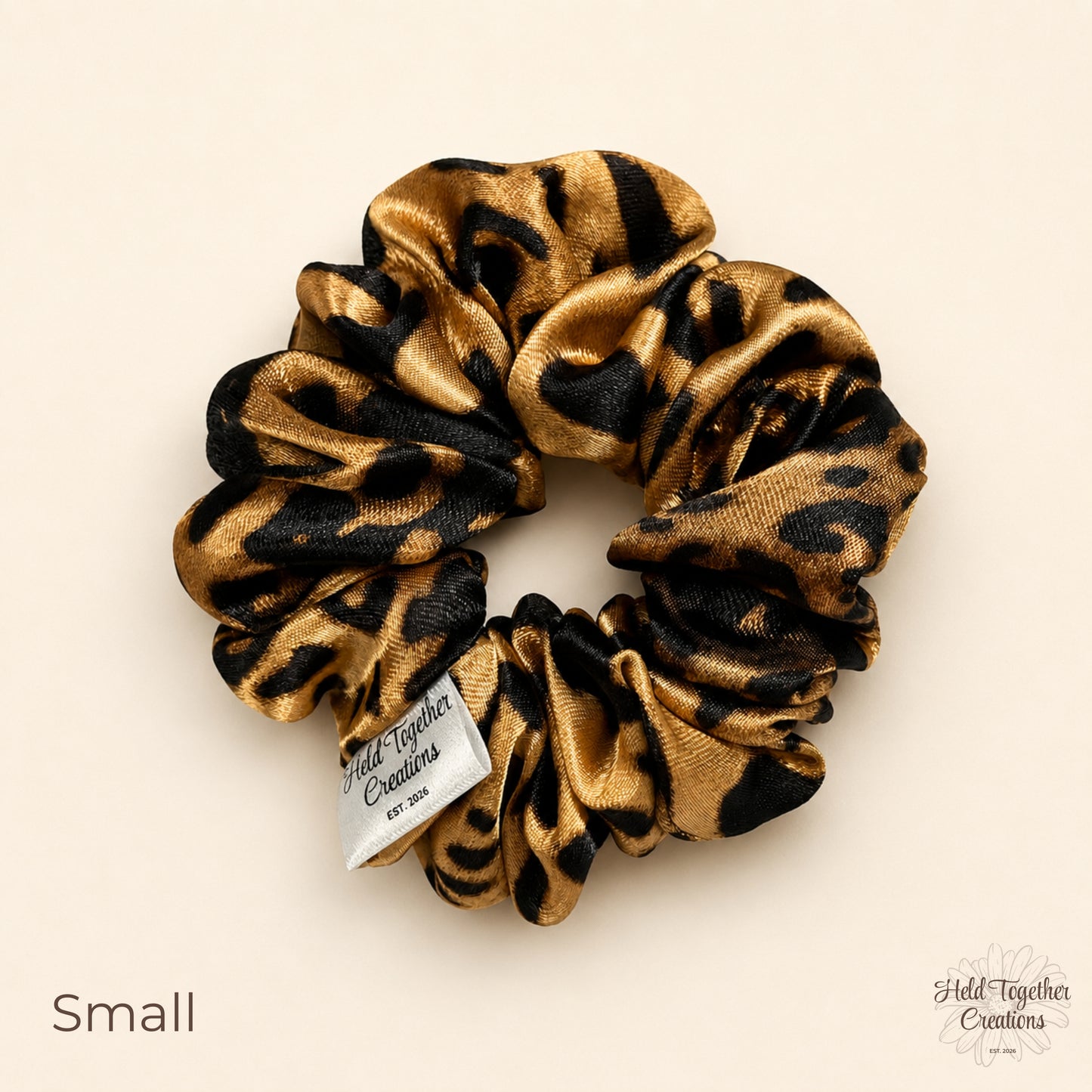 Small leopard satin scrunchie with glossy animal print fabric on a soft neutral background.