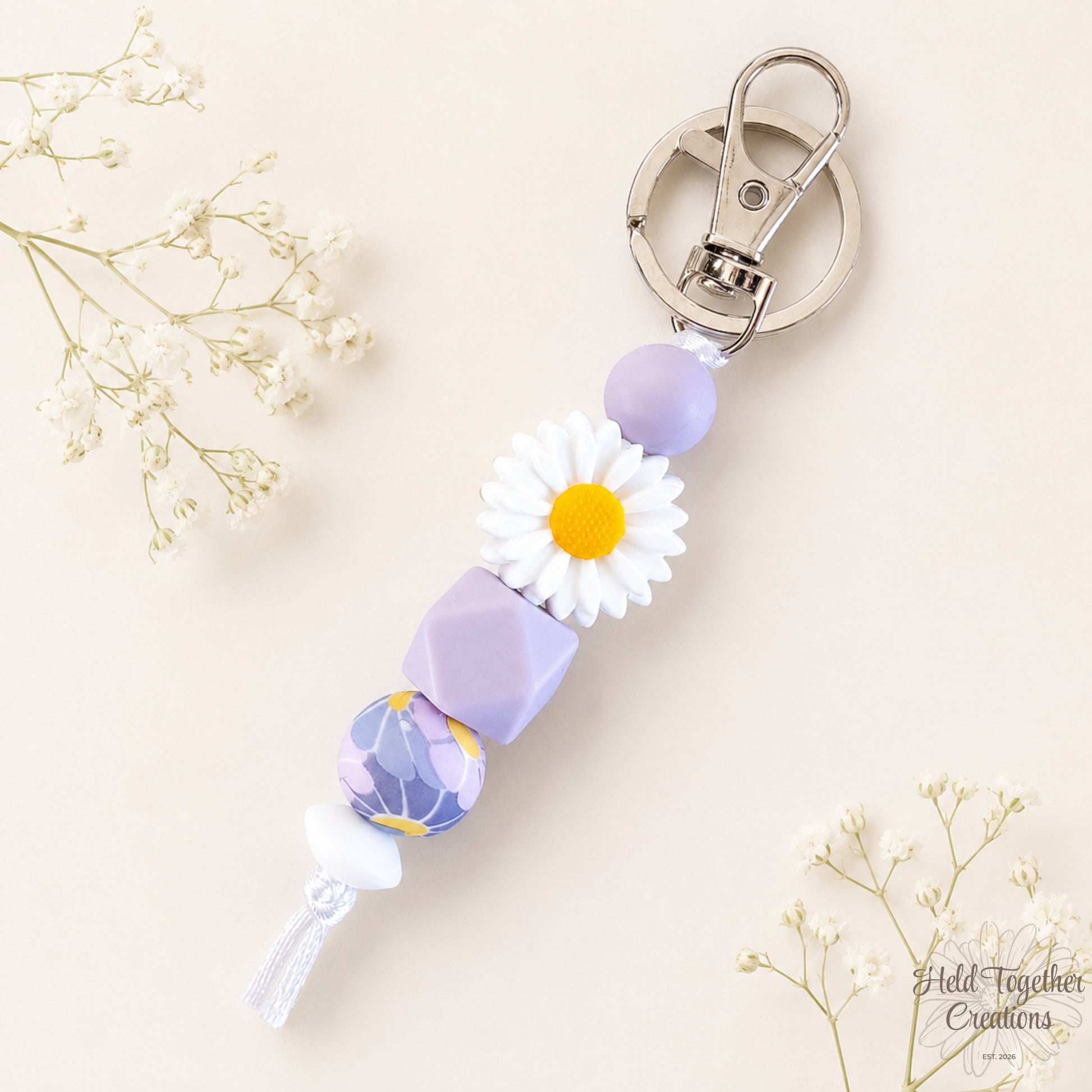 Lilac daisy silicone bead keyring with white daisy bead, lilac beads and silver keyring hardware on a soft neutral background.