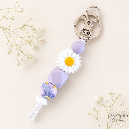 Lilac daisy silicone bead keyring with white daisy bead, lilac beads and silver keyring hardware on a soft neutral background.
