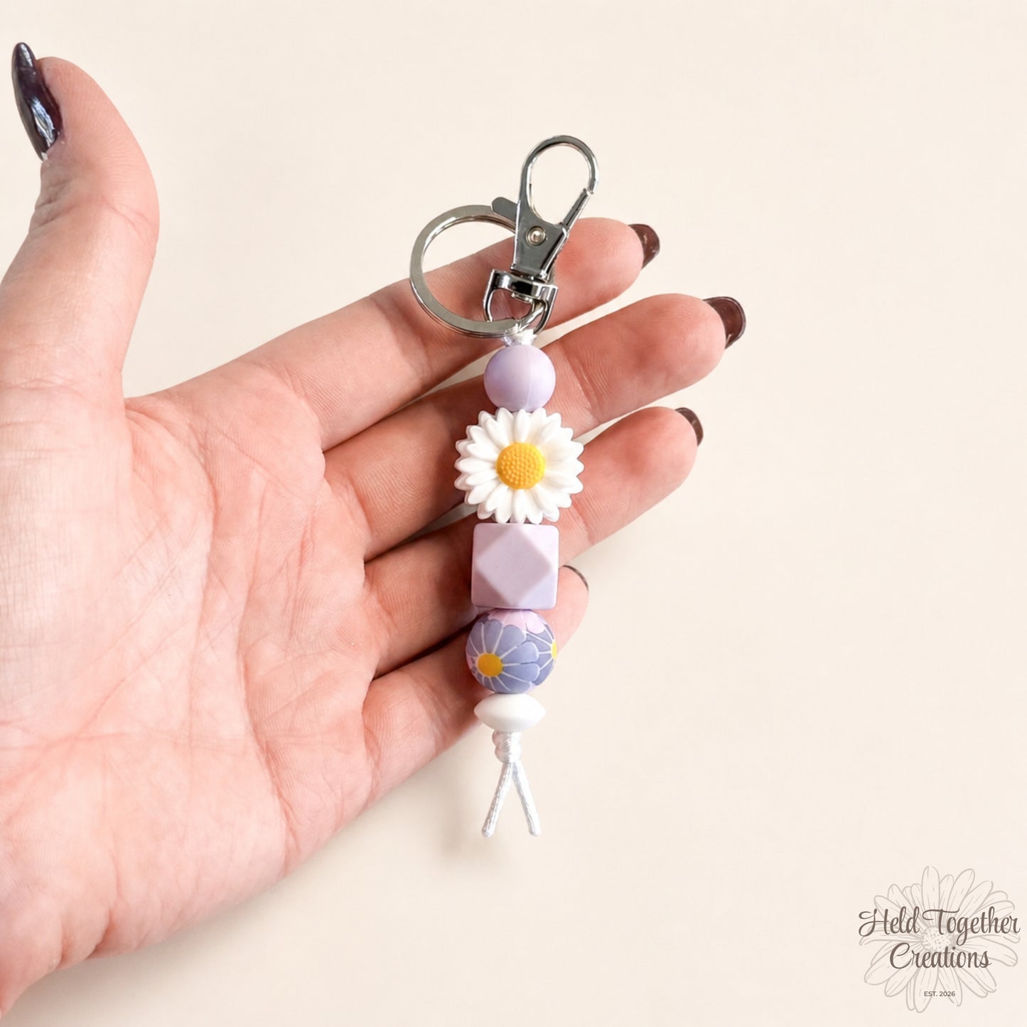 Lilac daisy silicone bead keyring with white daisy bead, lilac beads and silver keyring hardware on a soft neutral background.