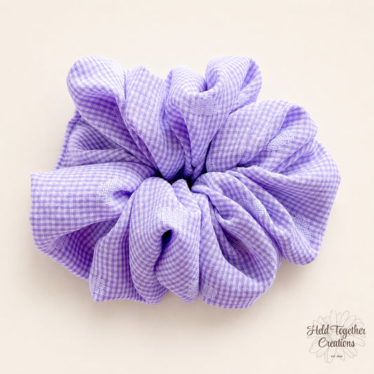 Lilac and white check handmade fabric scrunchie on a soft ivory background.