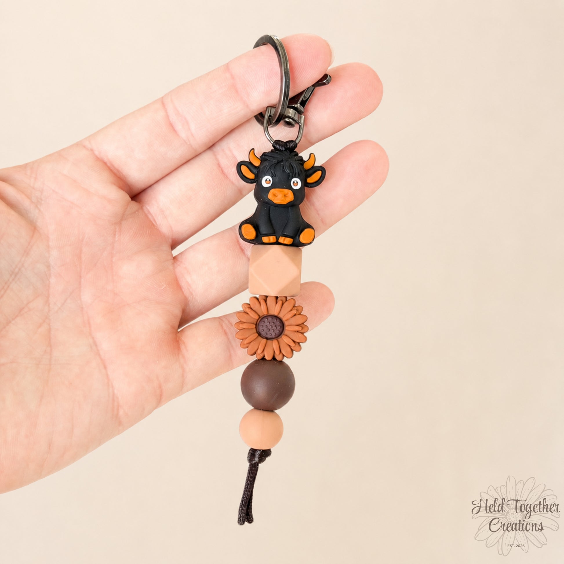 Hand holding a keychain with a cow charm and beads on a beige background