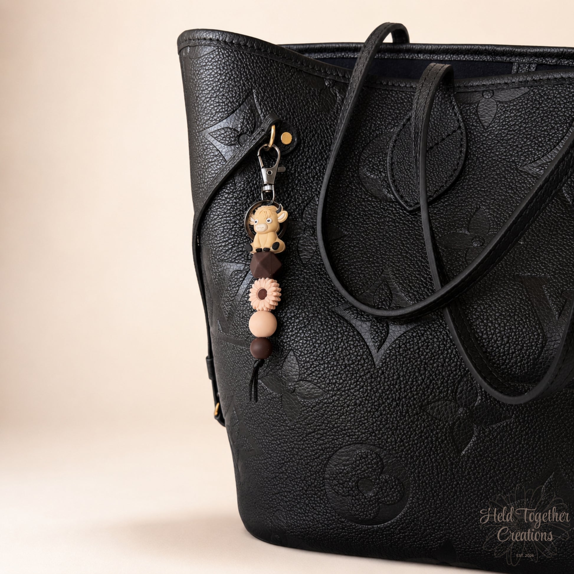 Black textured handbag with a decorative keychain on a beige background