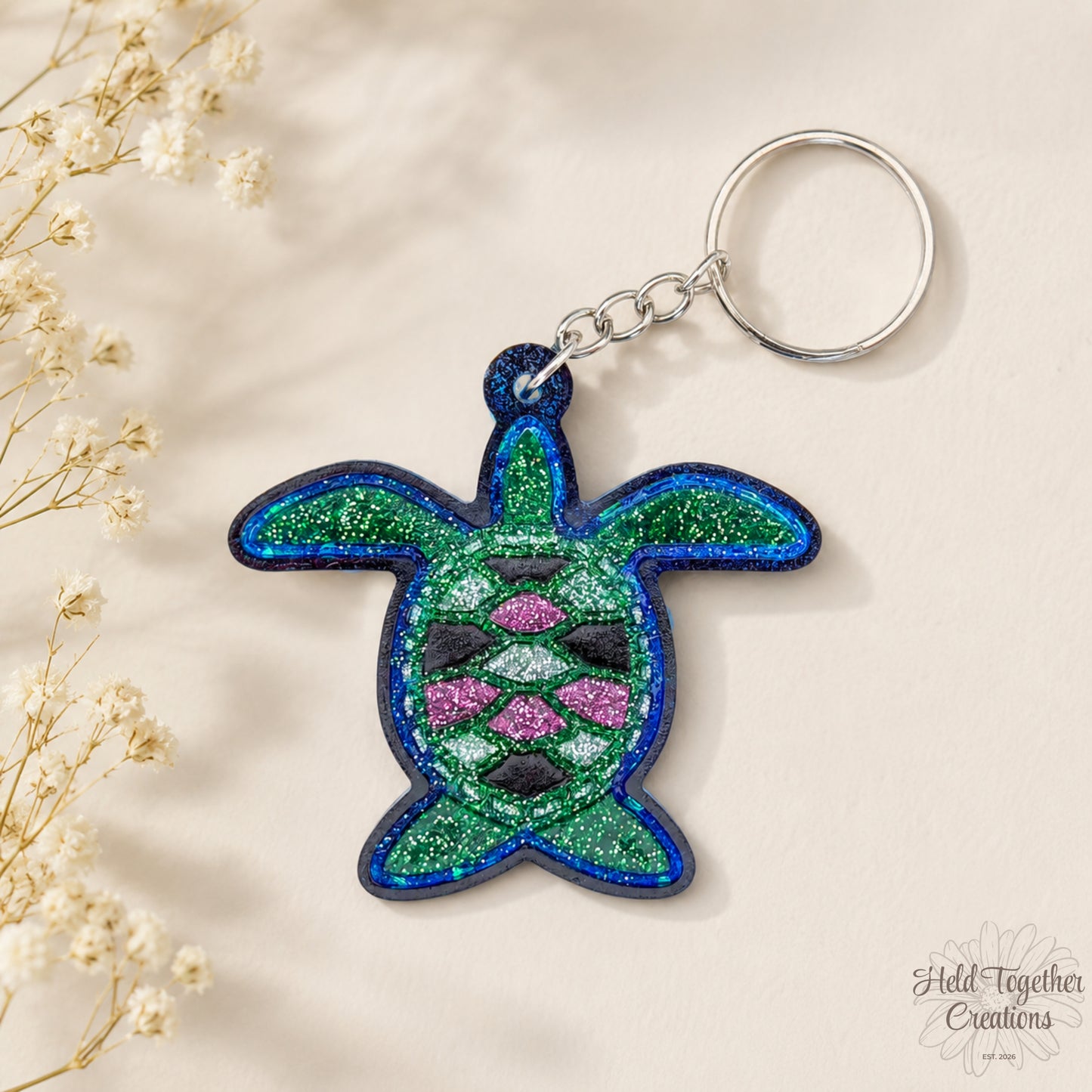 Handmade turtle resin keyring with green, blue and pink glitter details on a soft neutral background.