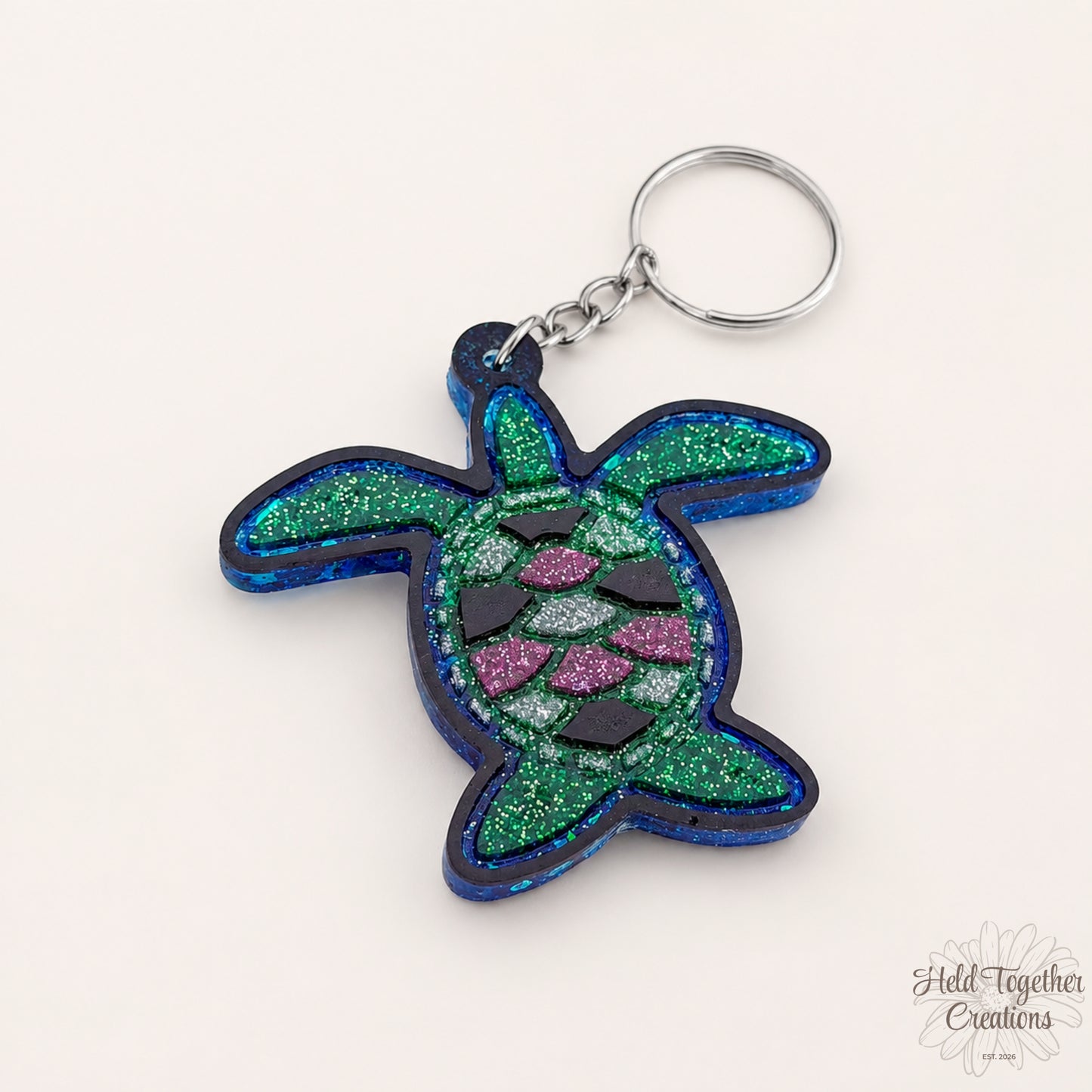 Handmade turtle resin keyring with green, blue and pink glitter details on a soft neutral background.