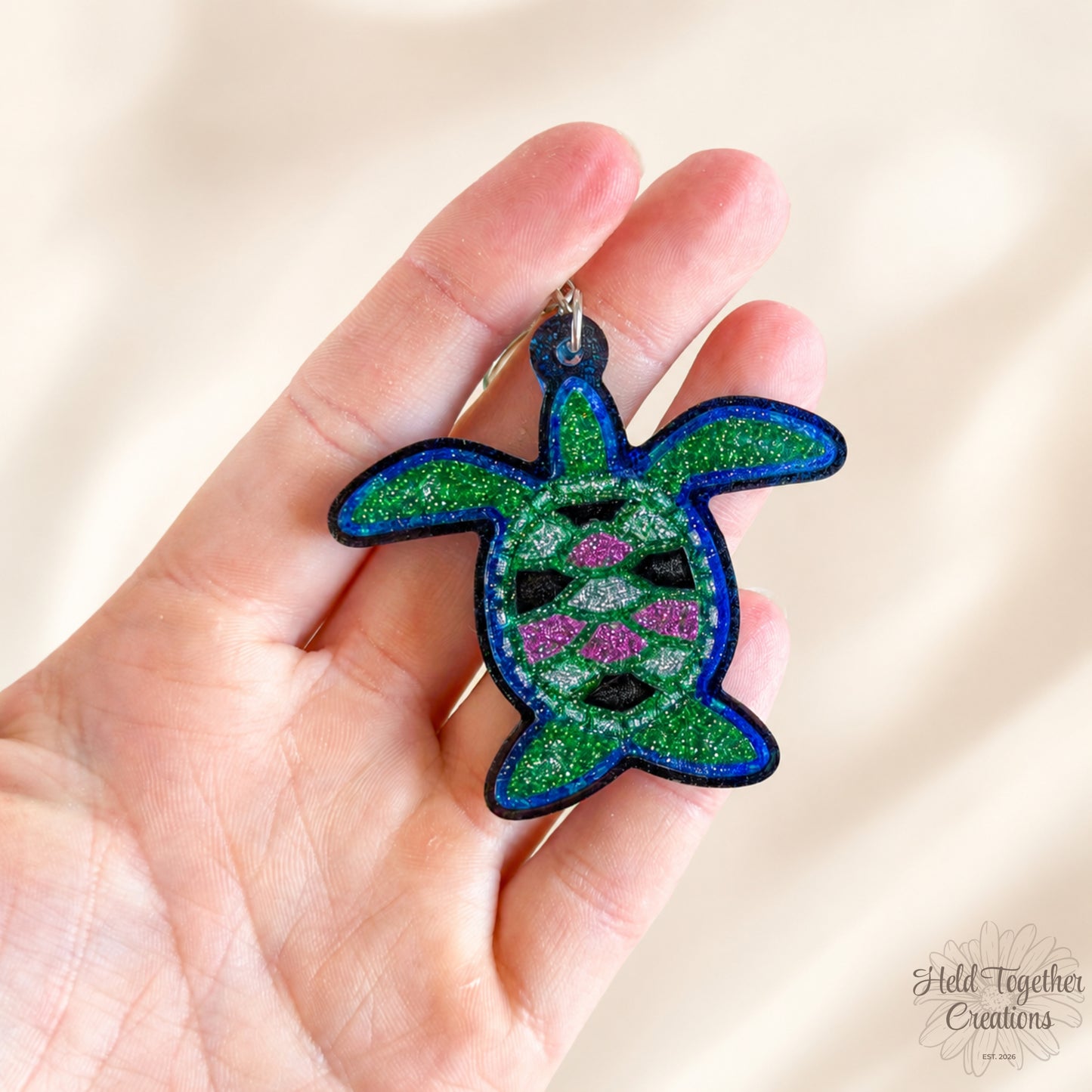 Handmade turtle resin keyring with green, blue and pink glitter details on a soft neutral background.