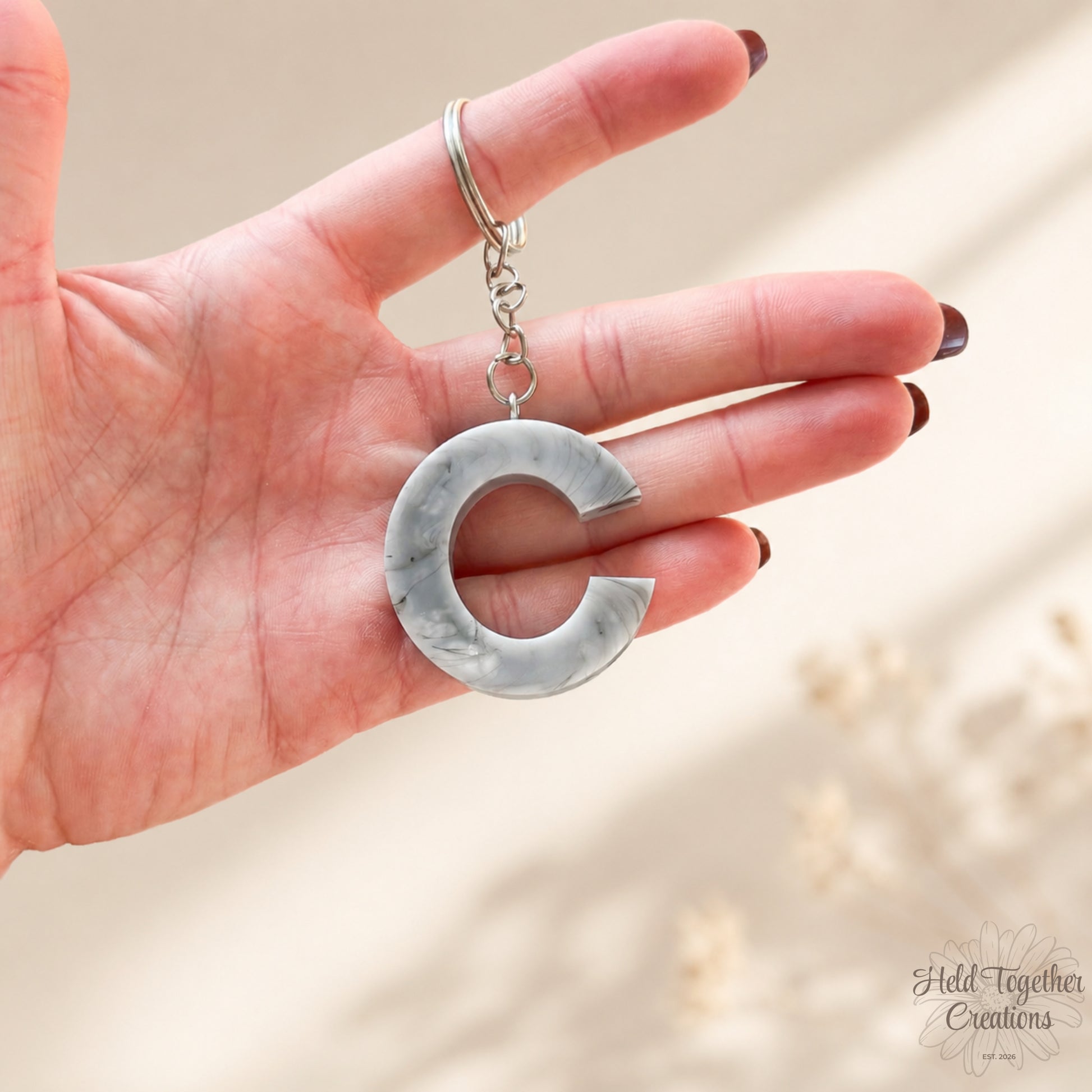 Hand holding a silver keychain with a unique design against a neutral background
