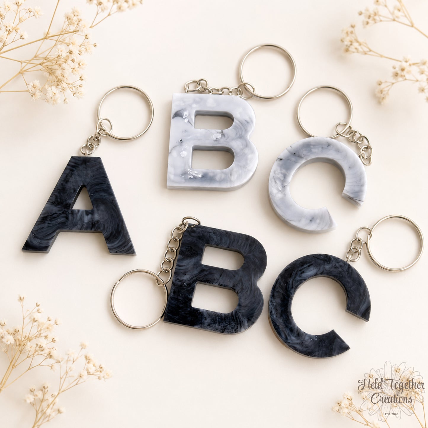 Marble-textured letter keychains on a light background with dried flowers.