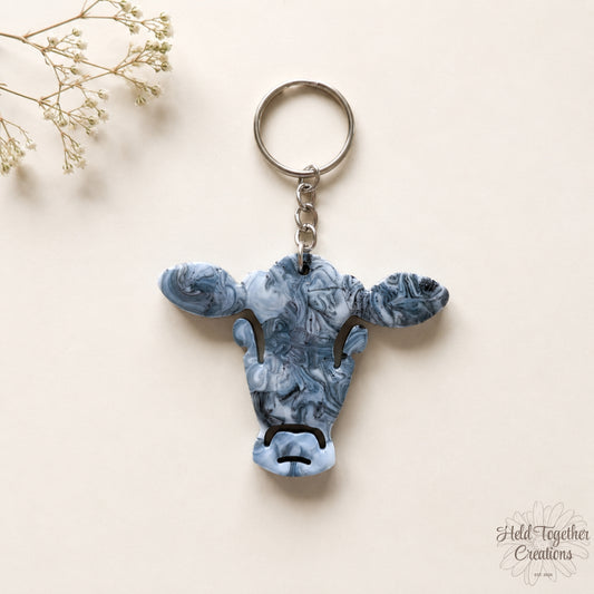 Handmade black, white and grey marble resin cow keyring with silver hardware on a soft neutral background.