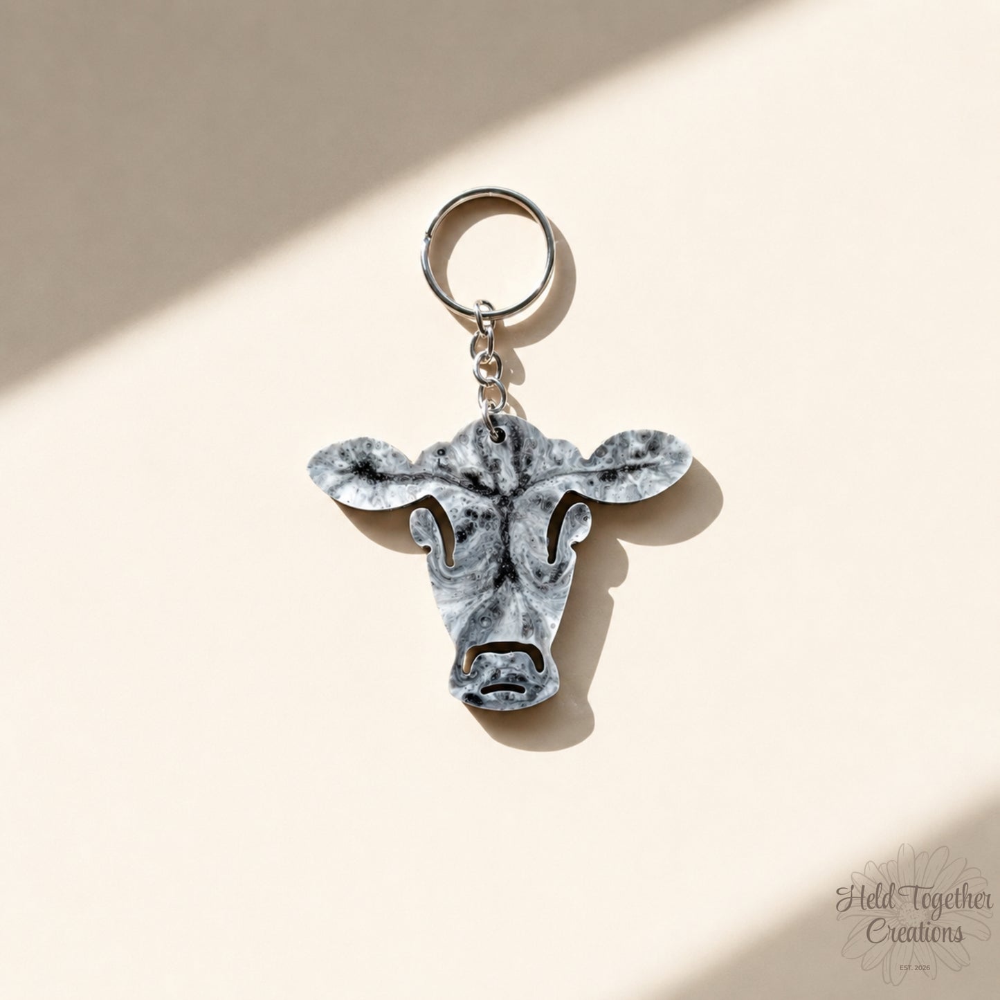 Handmade black, white and grey marble resin cow keyring with silver hardware on a soft neutral background.