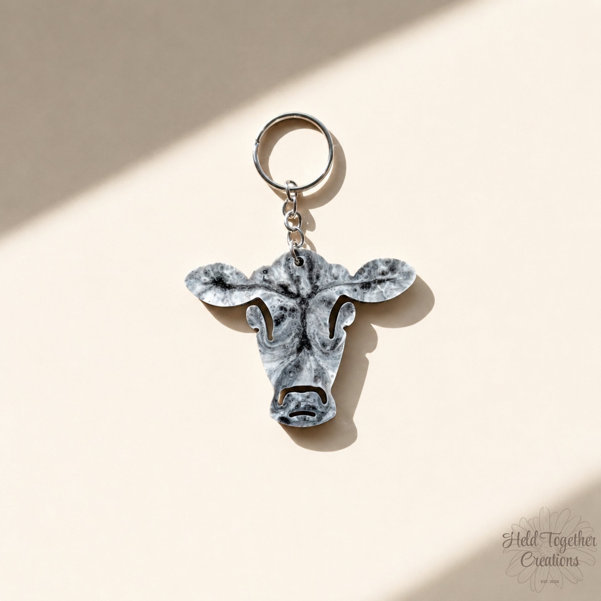 Handmade black, white and grey marble resin cow keyring with silver hardware on a soft neutral background.