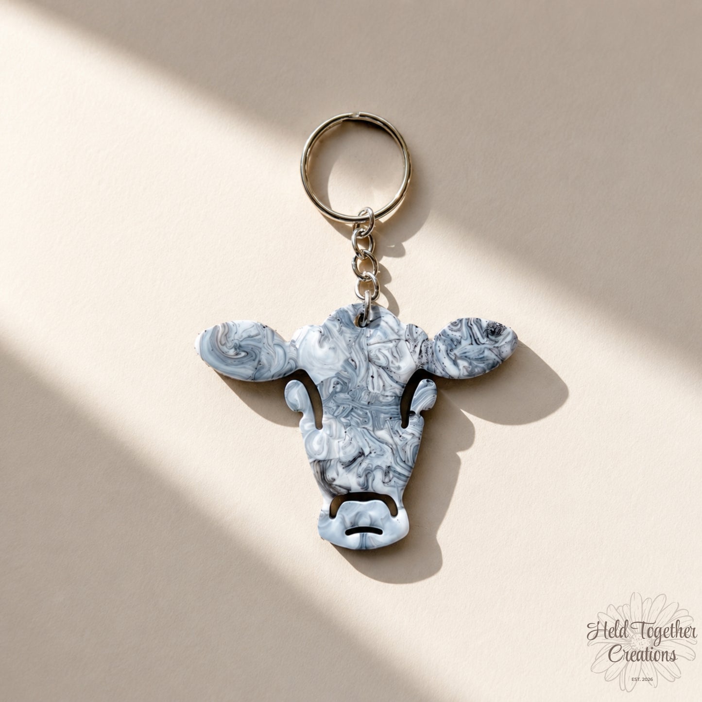 Handmade black, white and grey marble resin cow keyring with silver hardware on a soft neutral background.