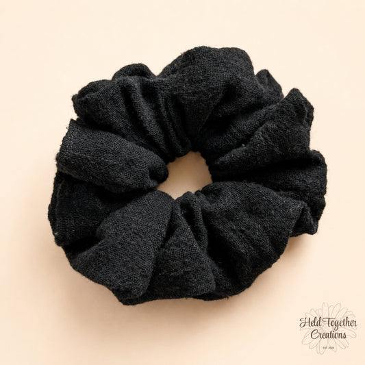 Black linen-style handmade scrunchie on a warm ivory background.