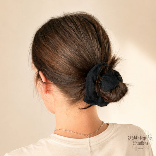 Black linen-style handmade scrunchie on a warm ivory background.
