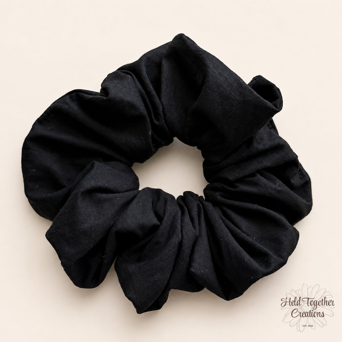 Black handmade cotton scrunchie on a warm ivory background.
