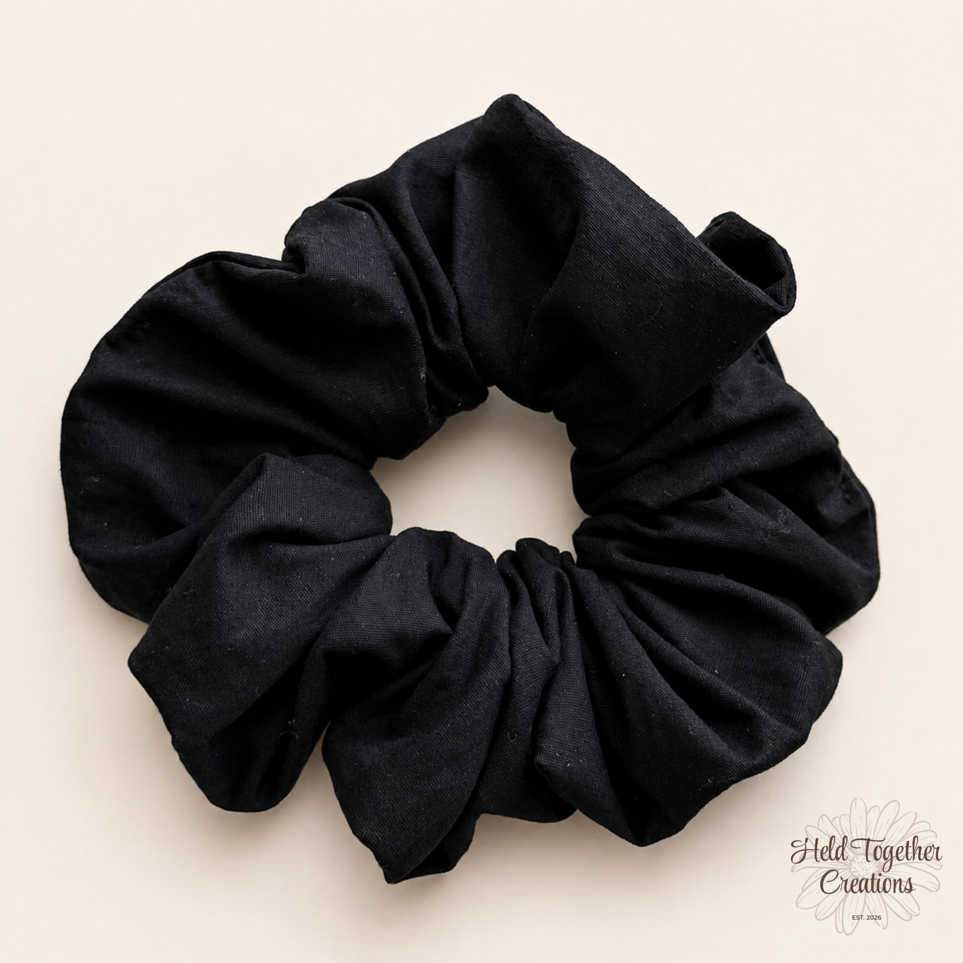 Black handmade cotton scrunchie on a warm ivory background.