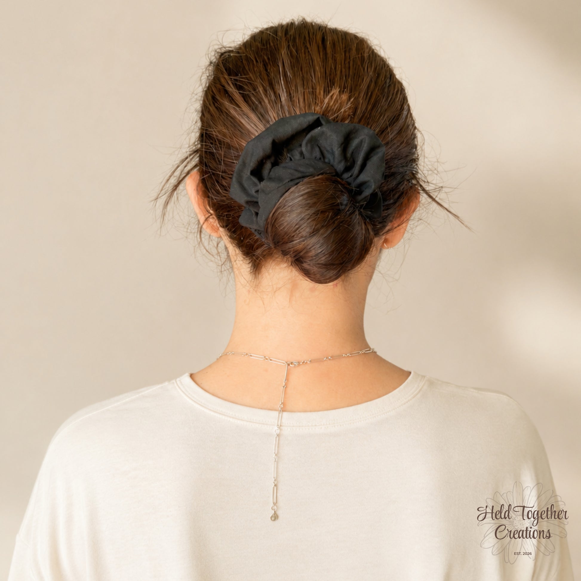 Black handmade cotton scrunchie on a warm ivory background.