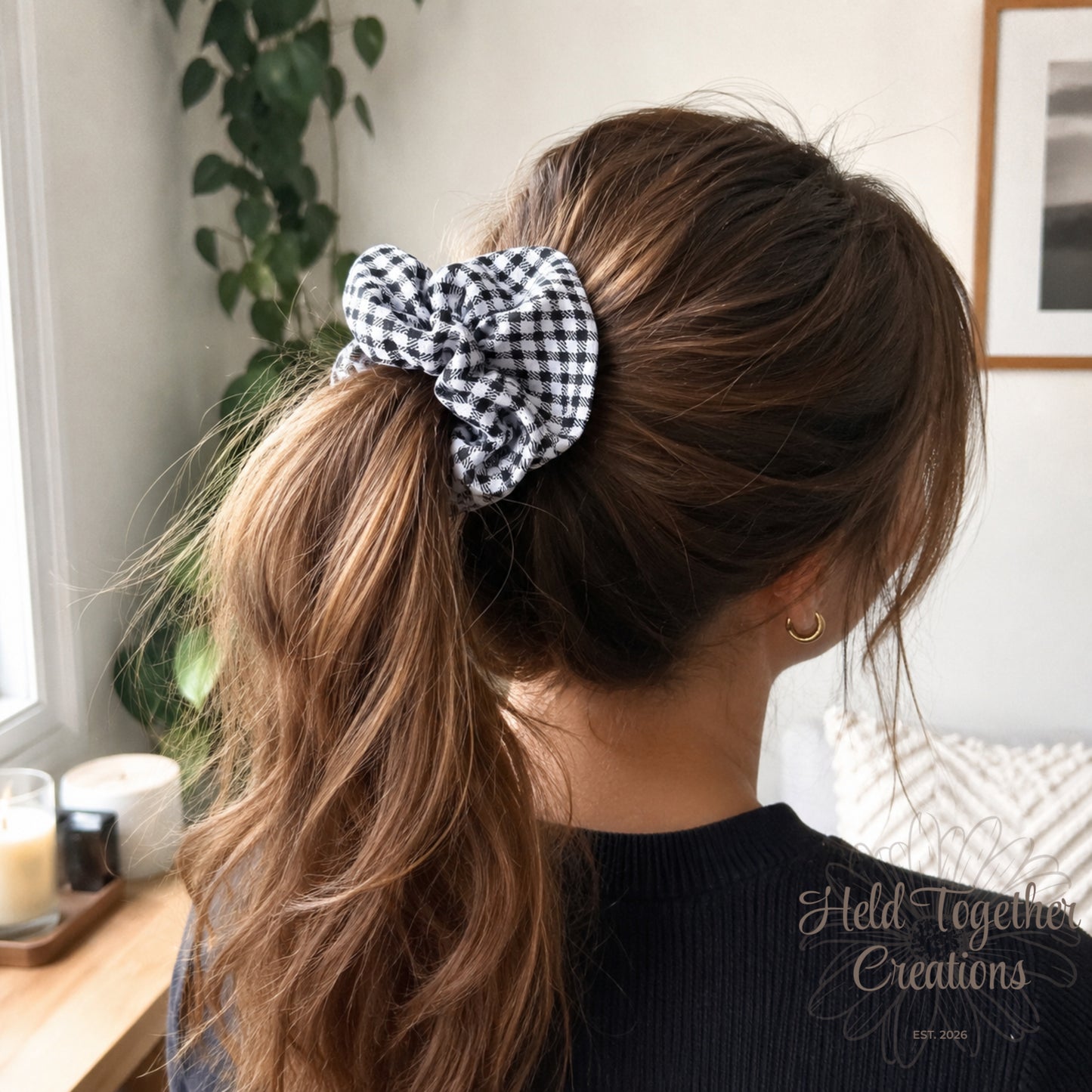 Person with a ponytail held with a checkered scrunchie, sitting indoors.