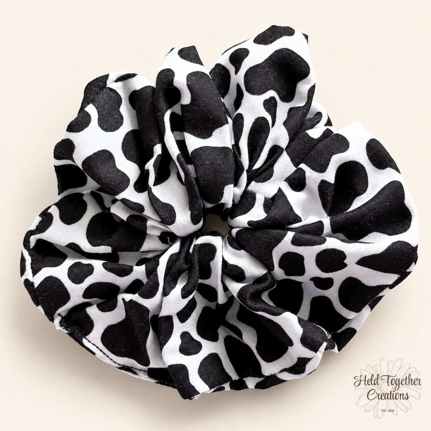 Black and white cow print handmade scrunchie on a warm neutral background.