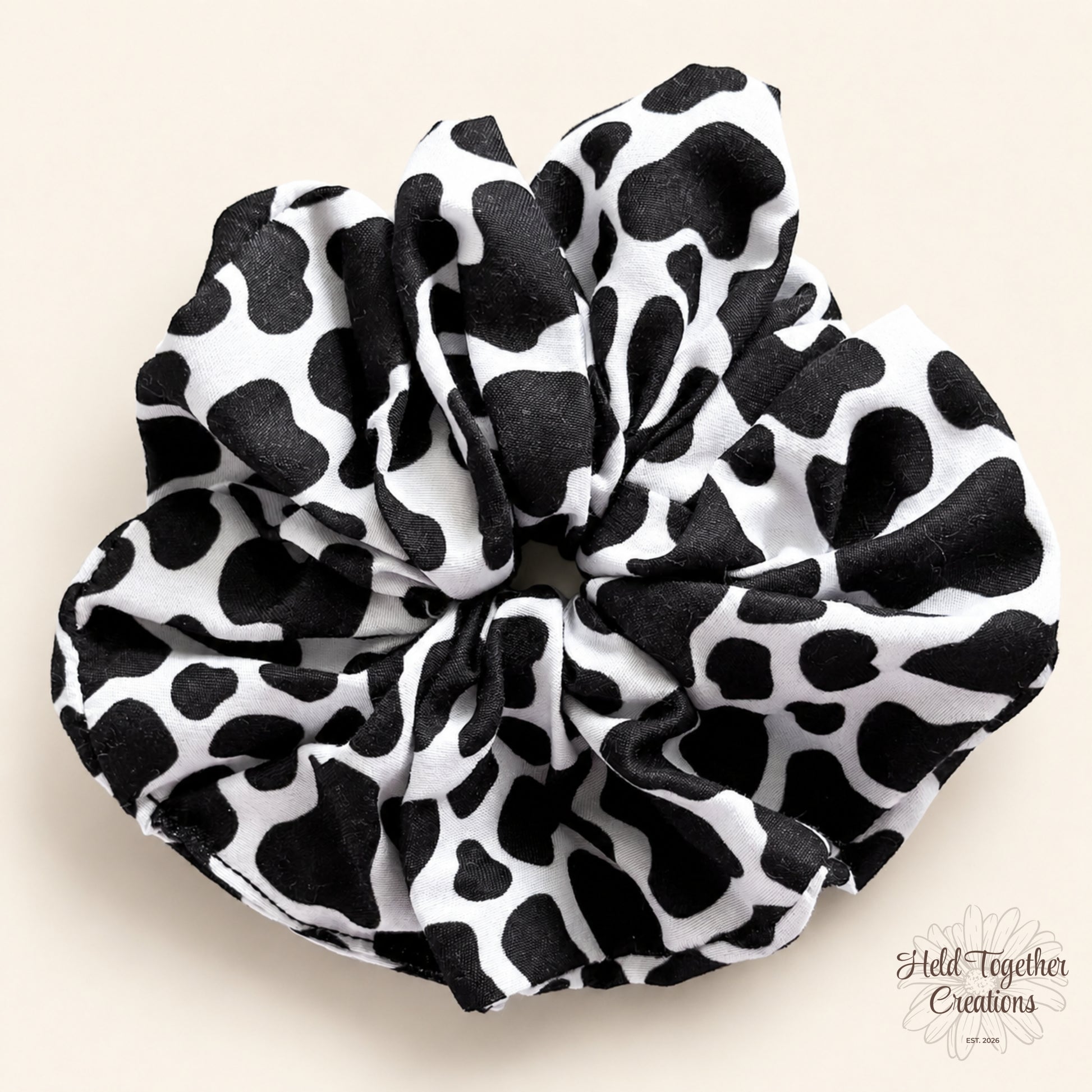 Black and white cow print handmade scrunchie on a warm neutral background.