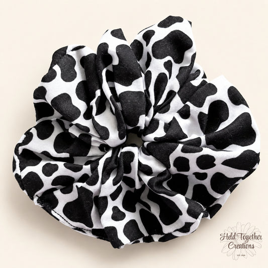 Black and white cow print handmade scrunchie on a warm neutral background.