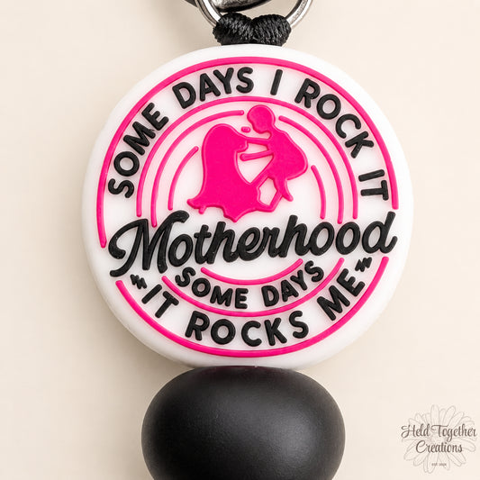 Handmade Motherhood Rocks silicone bead keyring with pink, black and white beads on a warm ivory background.
