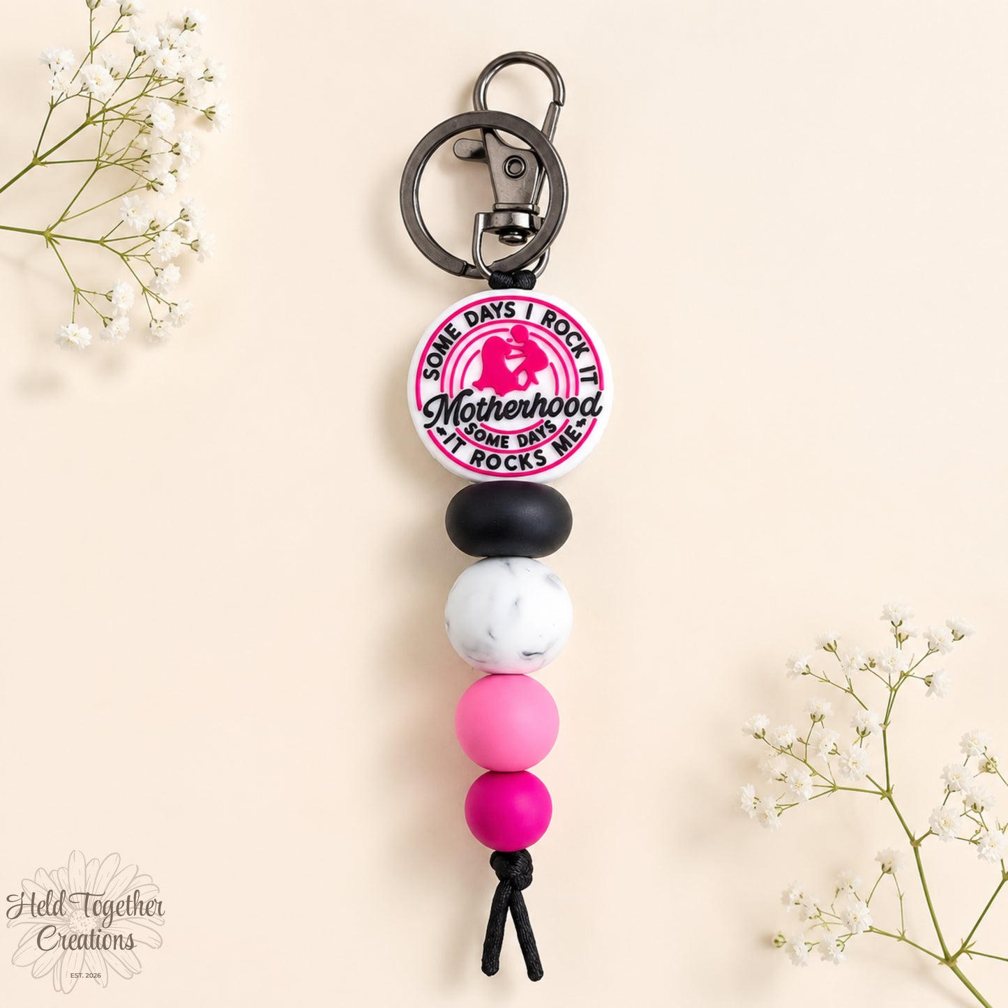 Handmade Motherhood Rocks silicone bead keyring with pink, black and white beads on a warm ivory background.