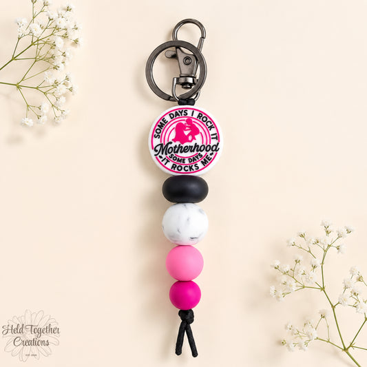 Handmade Motherhood Rocks silicone bead keyring with pink, black and white beads on a warm ivory background.