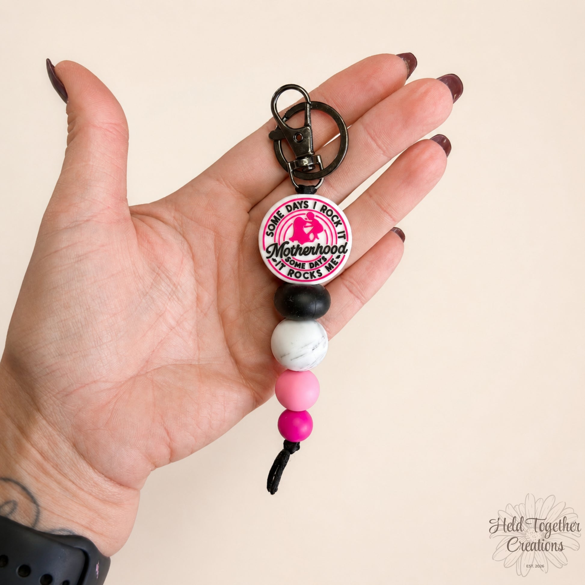 Handmade Motherhood Rocks silicone bead keyring with pink, black and white beads on a warm ivory background.