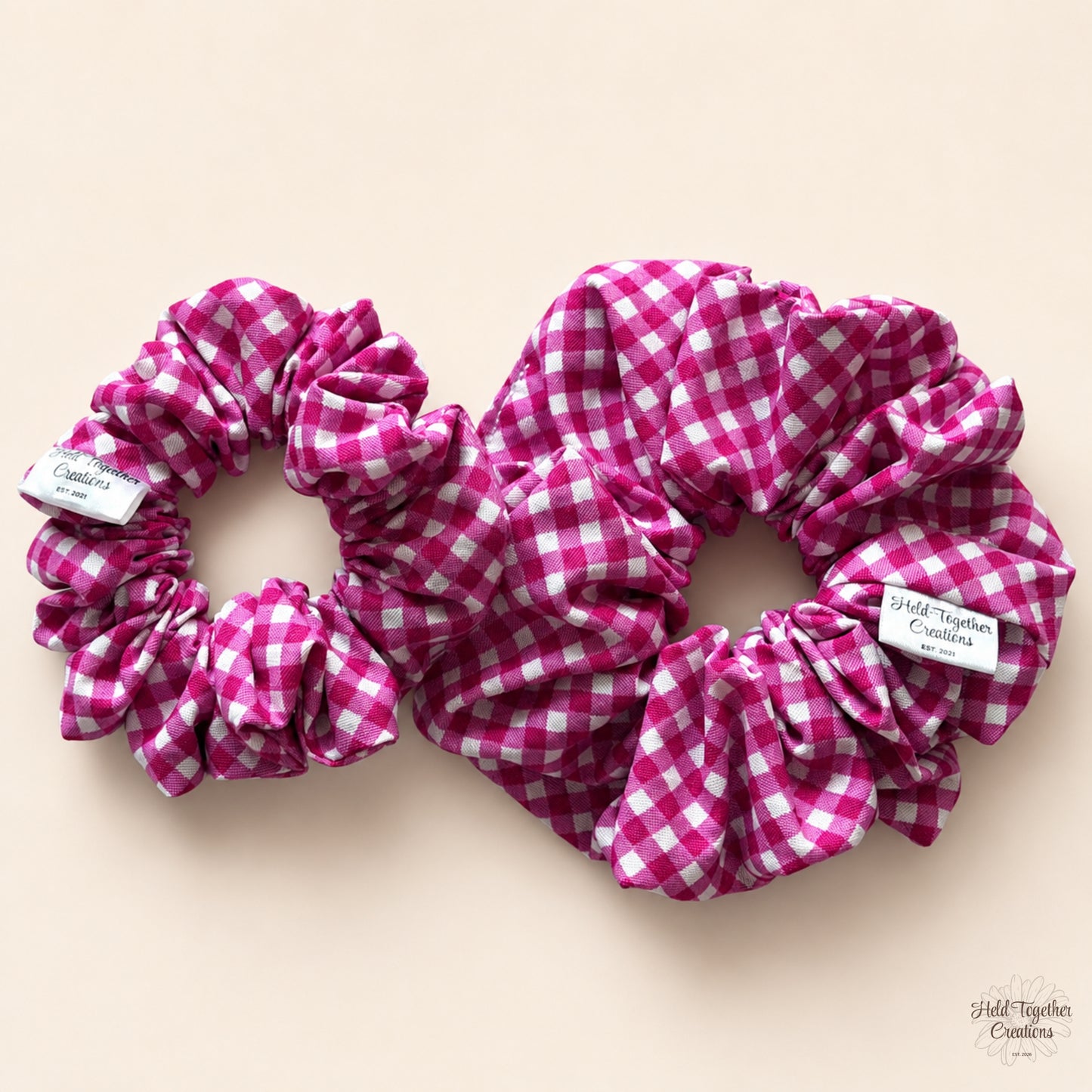 Small and large mulberry gingham scrunchies displayed together on a warm ivory background.