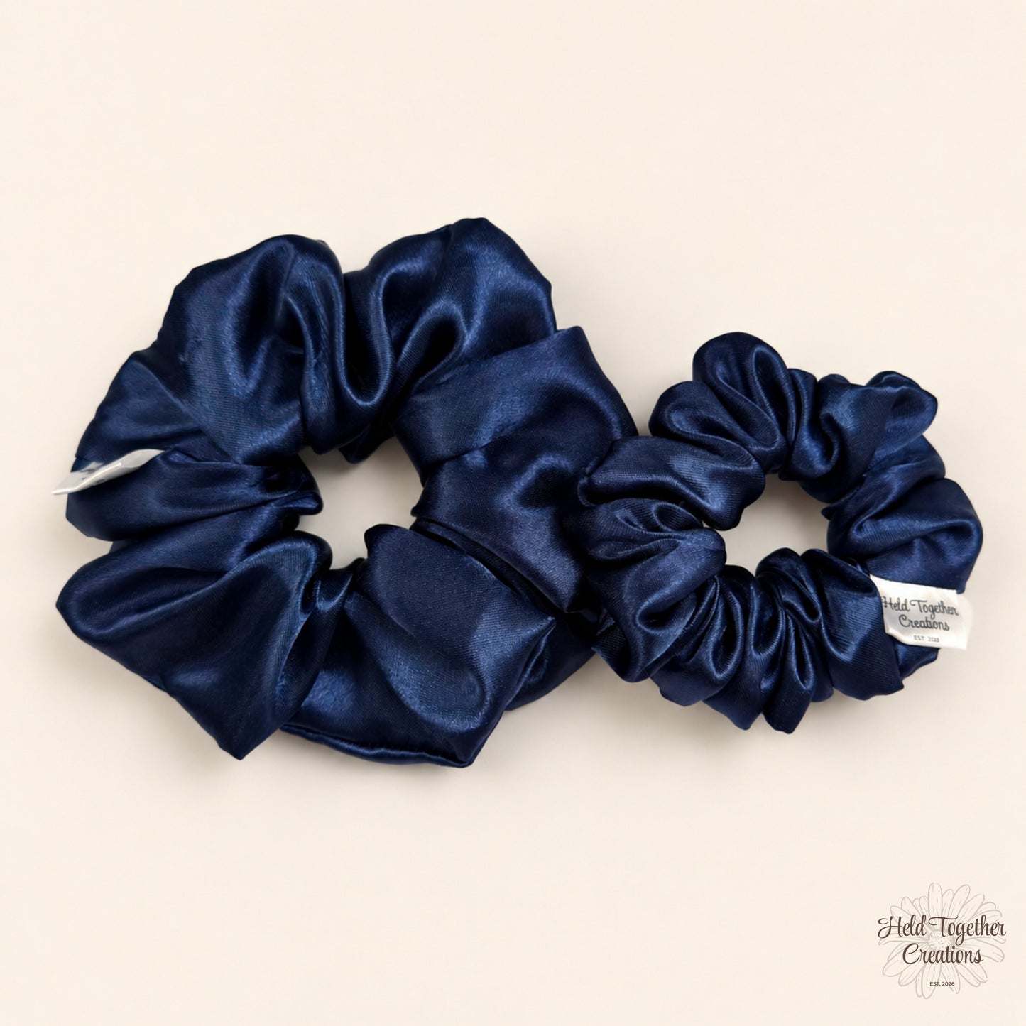 Small and large navy satin scrunchies side by side on a neutral background.