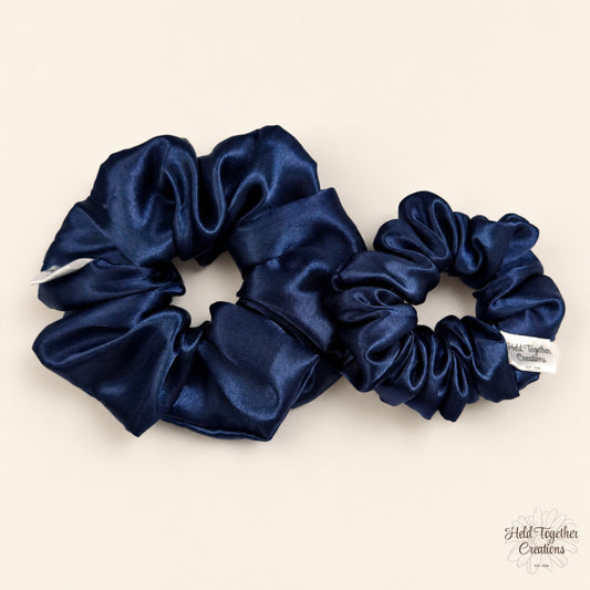 Small and large navy satin scrunchies side by side on a neutral background.