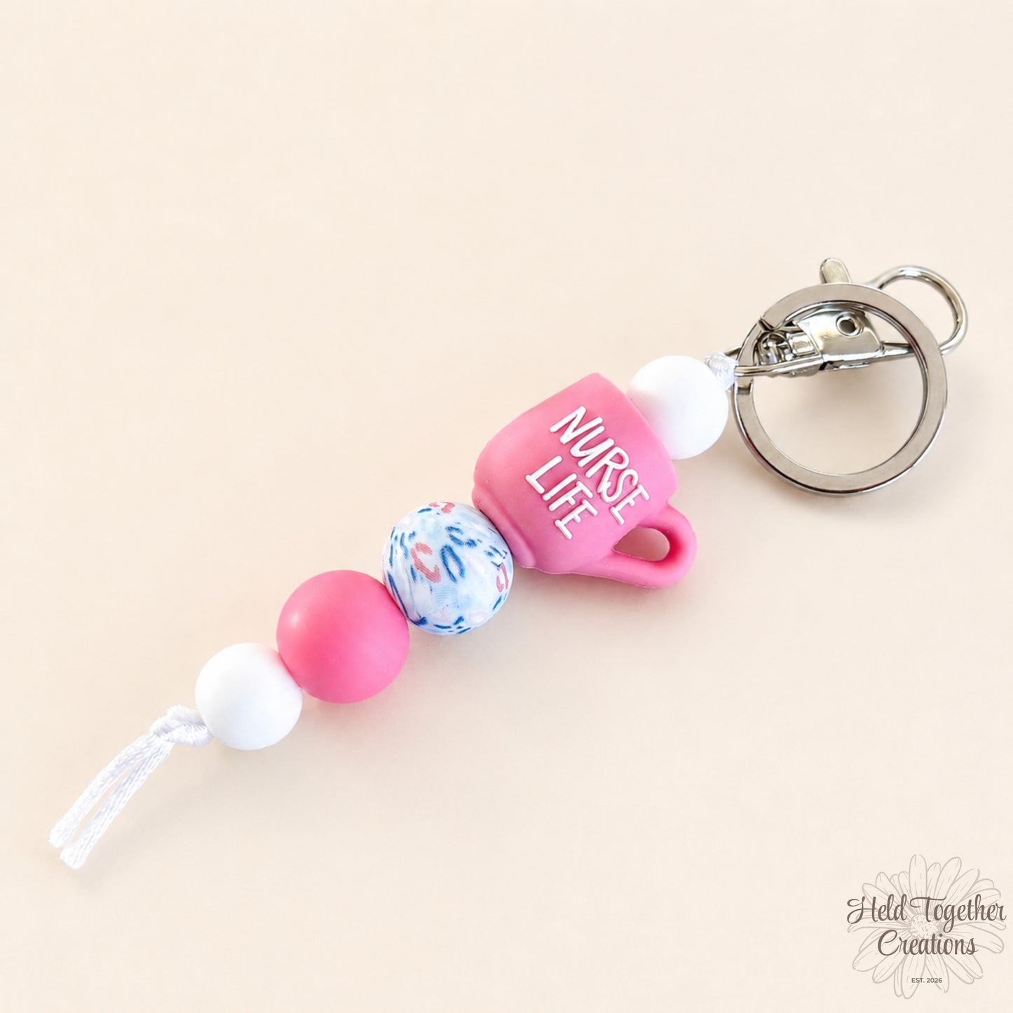 Handmade nurse life silicone bead keyrings with pink, teal and white silicone beads, medical charms and silver keyring hardware on a soft neutral background.