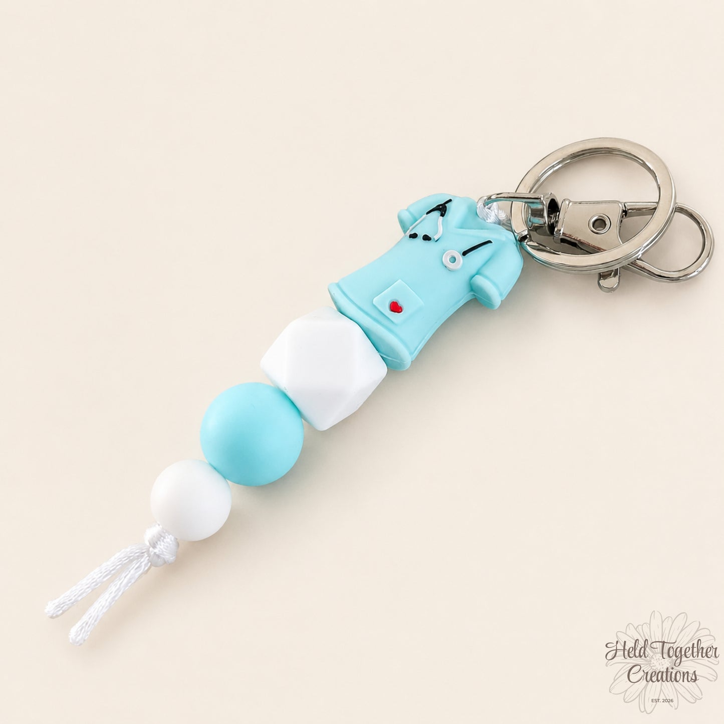 Handmade nurse life silicone bead keyrings with pink, teal and white silicone beads, medical charms and silver keyring hardware on a soft neutral background.