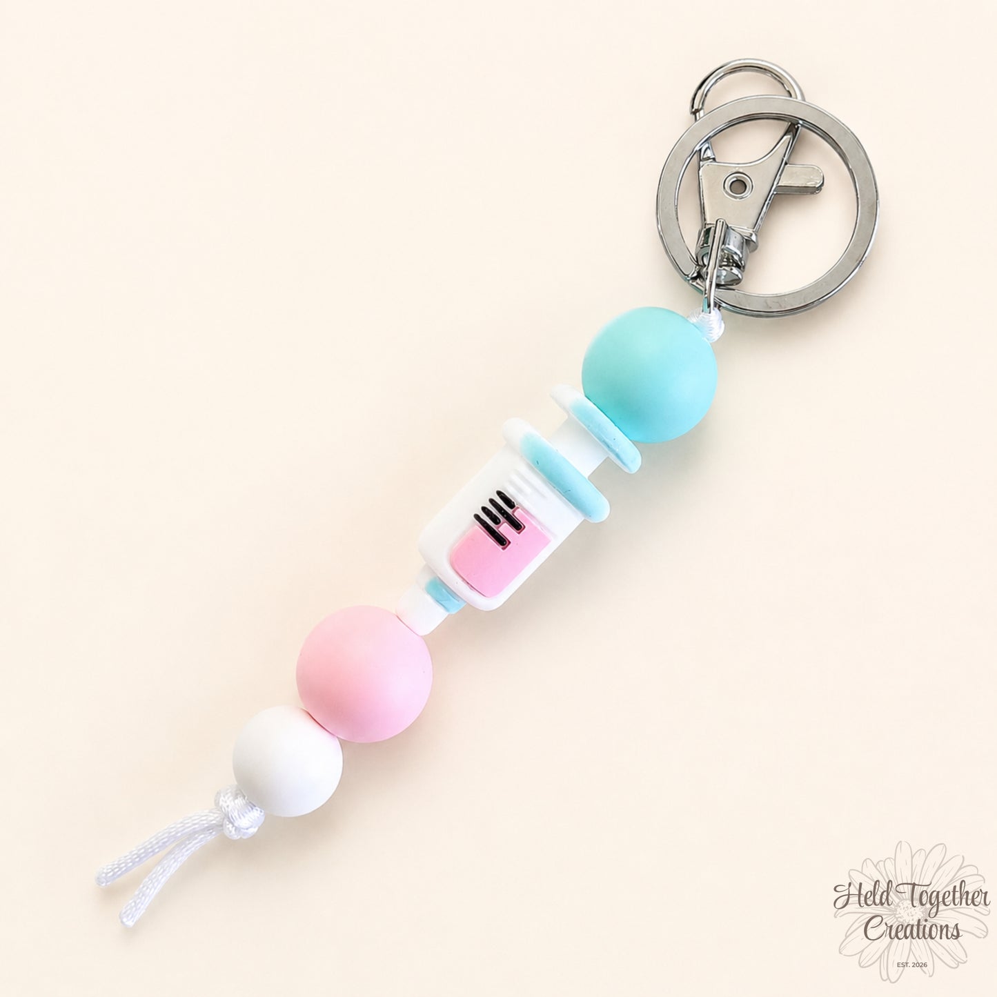 Handmade nurse life silicone bead keyrings with pink, teal and white silicone beads, medical charms and silver keyring hardware on a soft neutral background.