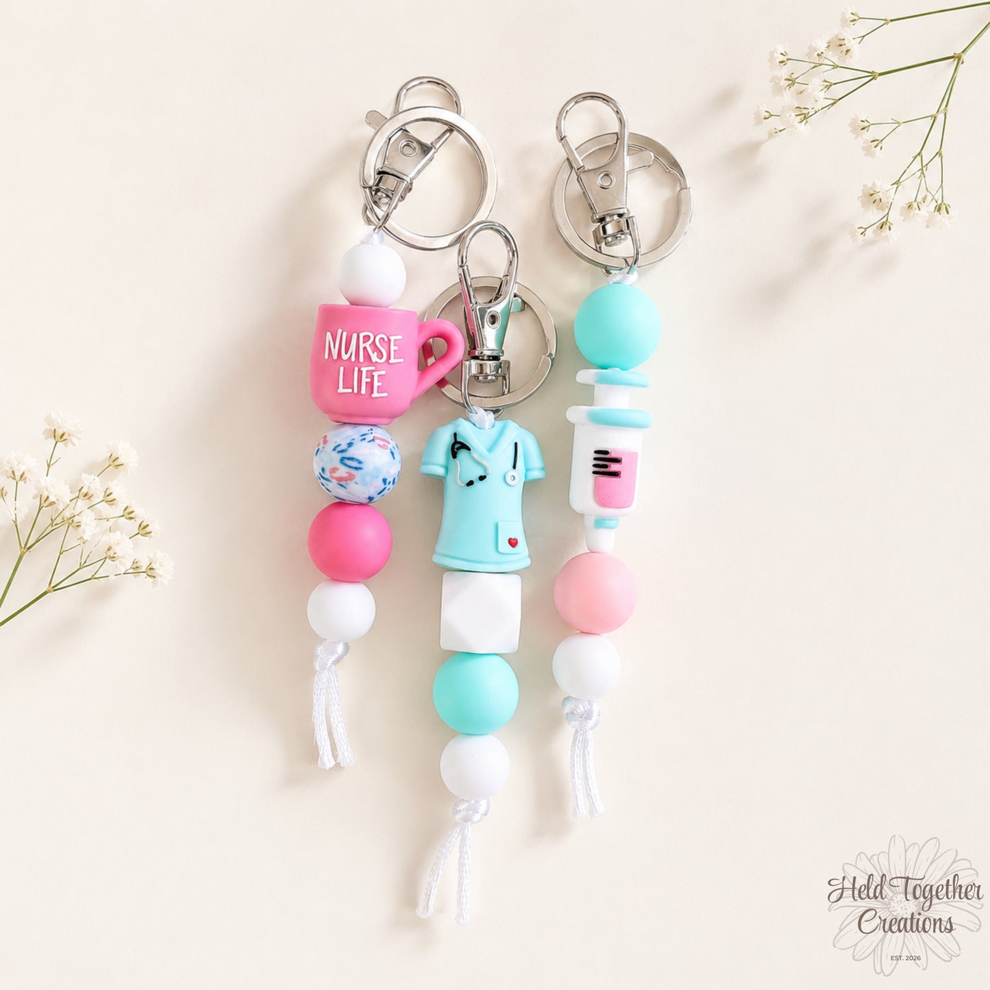 Handmade nurse life silicone bead keyrings with pink, teal and white silicone beads, medical charms and silver keyring hardware on a soft neutral background.