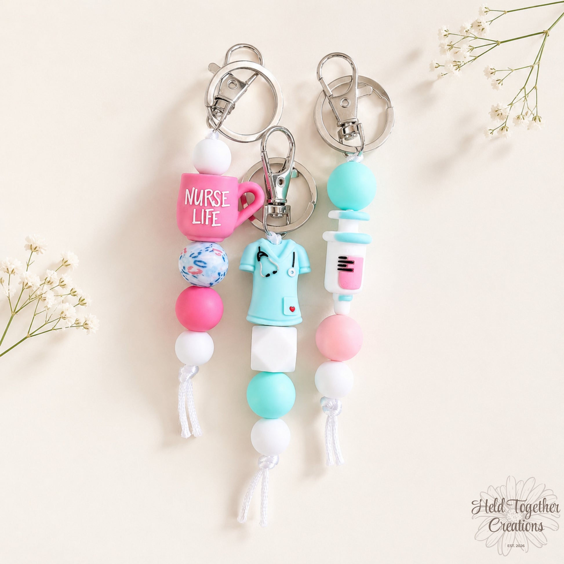 Handmade nurse life silicone bead keyrings with pink, teal and white silicone beads, medical charms and silver keyring hardware on a soft neutral background.