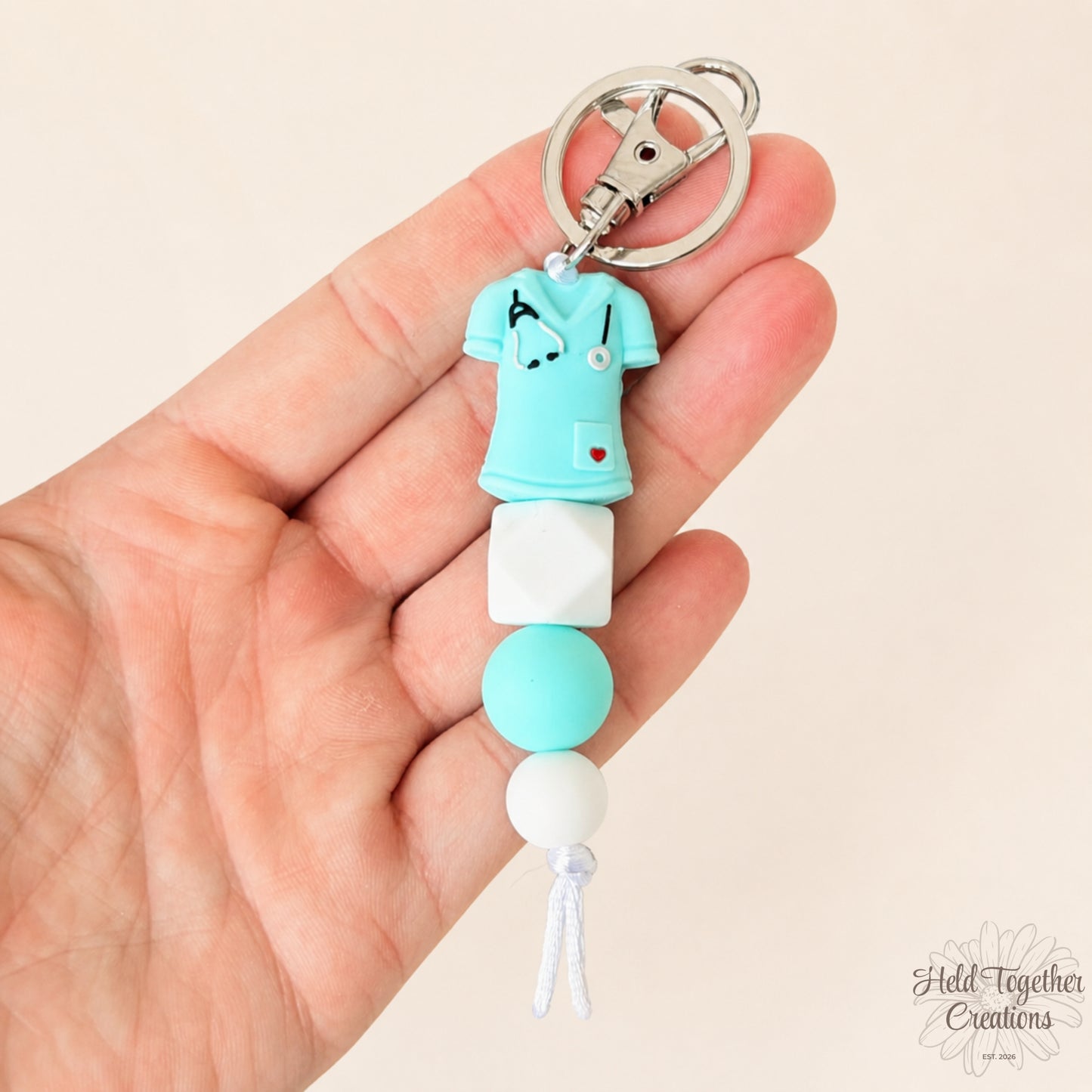 Handmade nurse life silicone bead keyrings with pink, teal and white silicone beads, medical charms and silver keyring hardware on a soft neutral background.