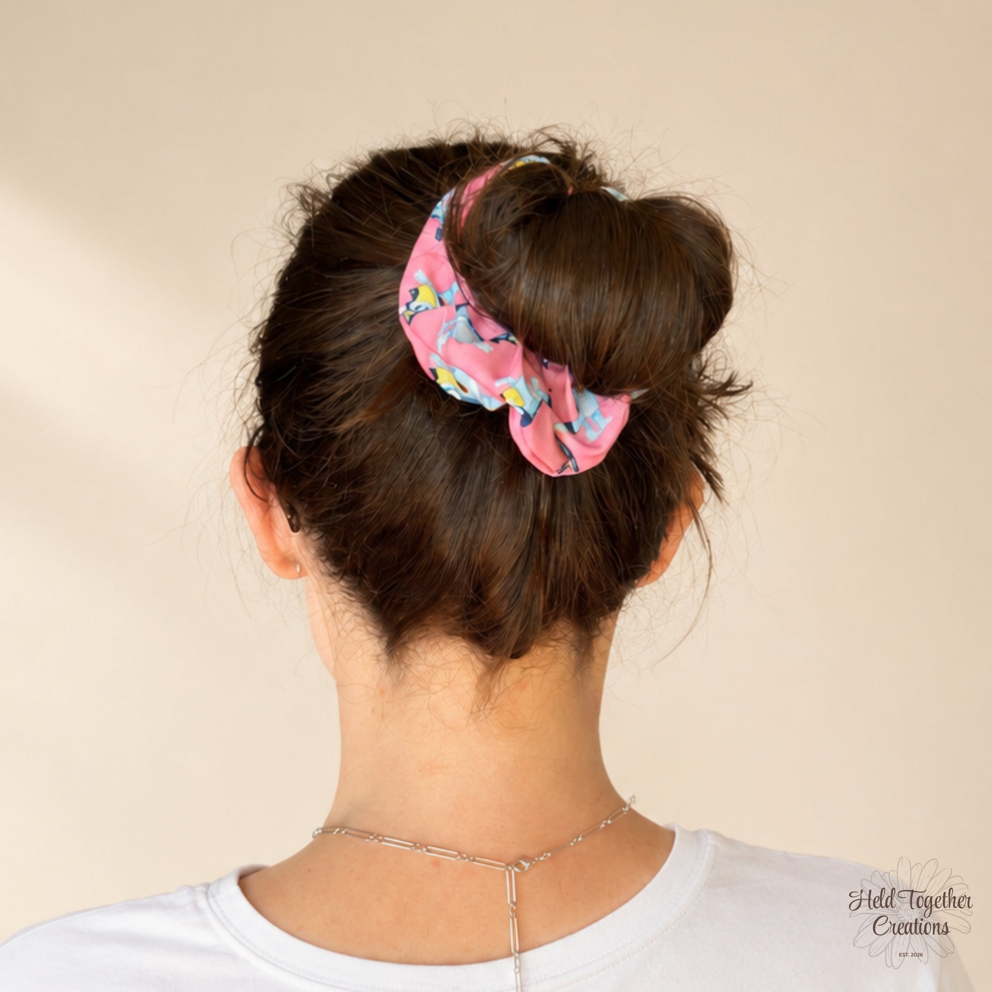 Party Pup Scrunchie worn around a messy bun, featuring colourful cartoon pups on bright pink fabric.