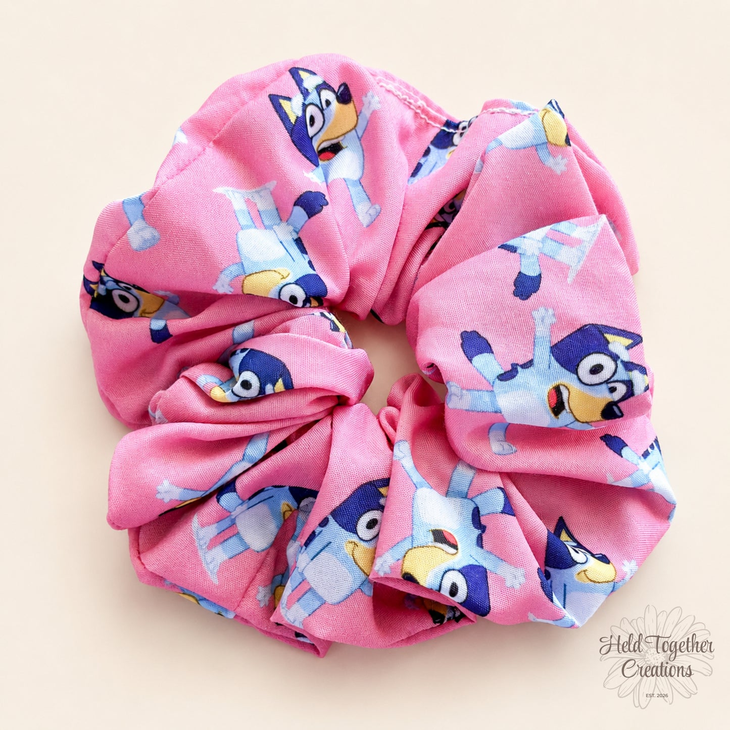 Party Pup handmade scrunchie in pink puppy-print fabric on a warm ivory background with Held Together Creations branding.