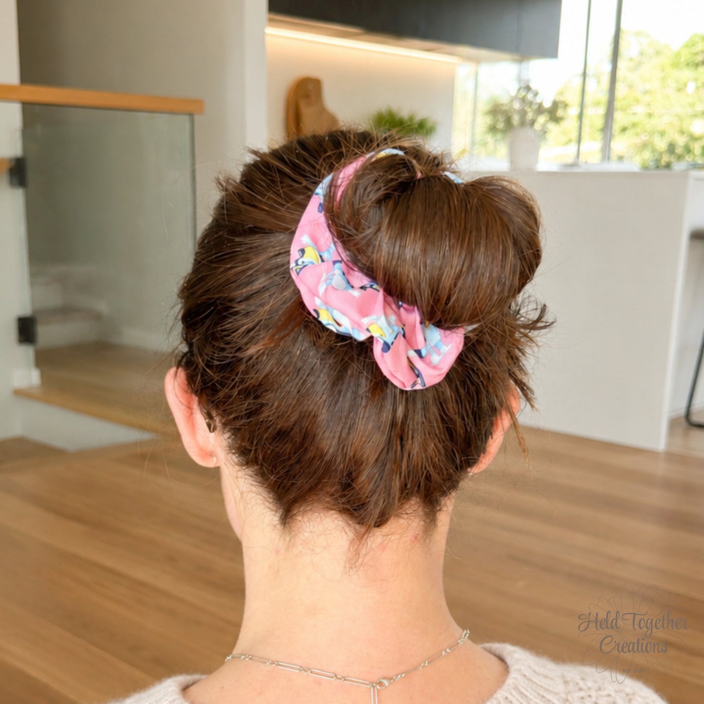 Party Pup scrunchie styled in a brown hair bun, showing the pink puppy-print fabric in a bright home setting.