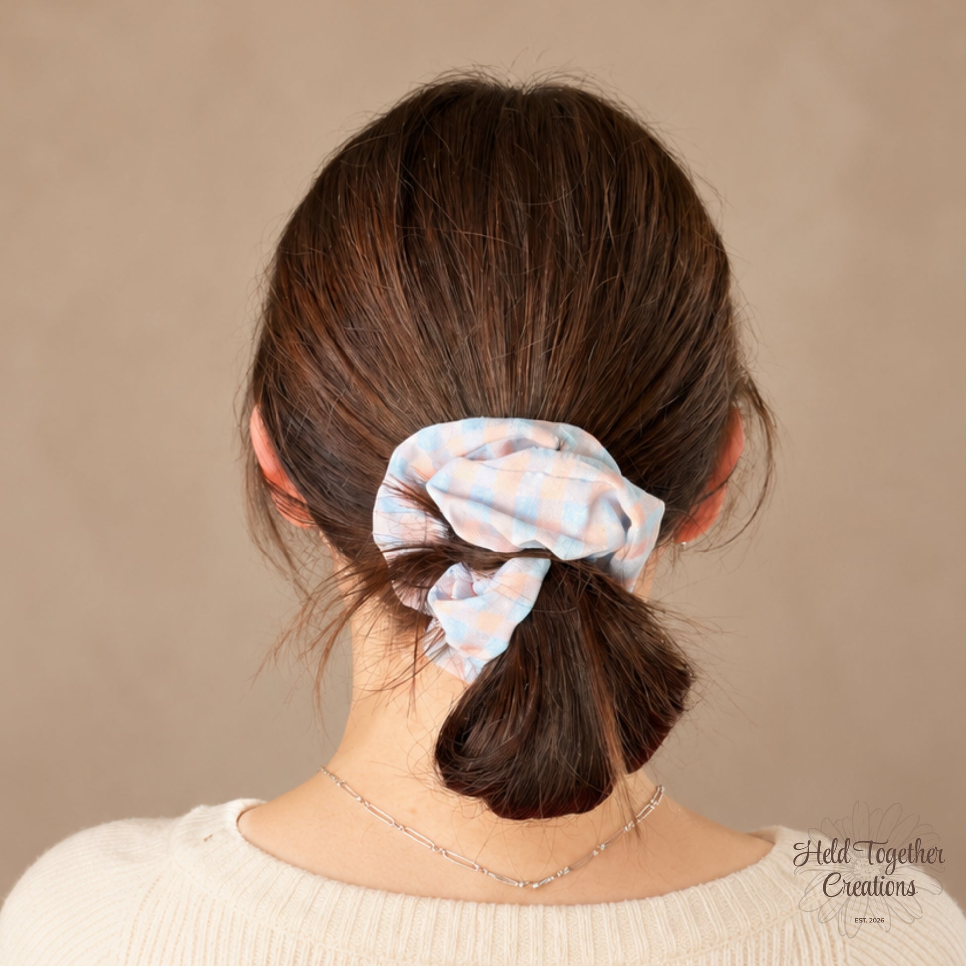 Pastel Picnic handmade fabric scrunchie with a soft pink and blue check pattern on a warm neutral background.