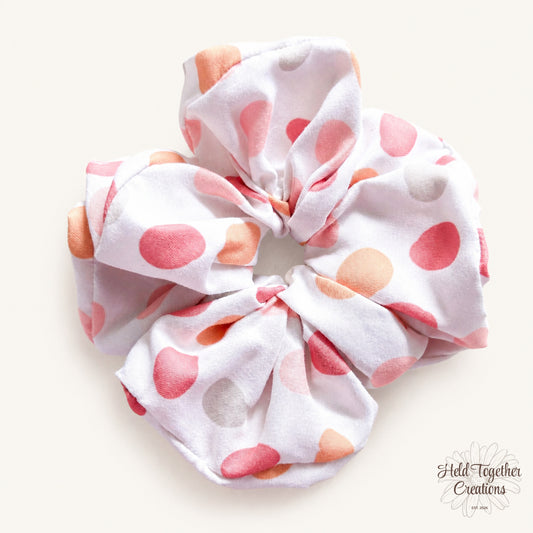 White handmade scrunchie with peach, coral, pink and neutral spot pattern by Held Together Creations.