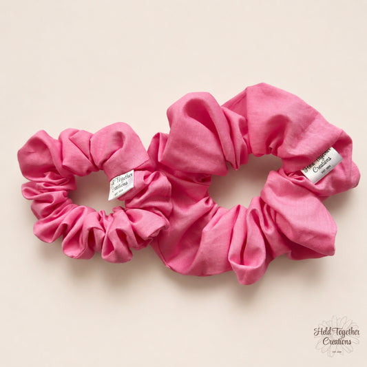 Small and large pink cotton scrunchies on a warm neutral background