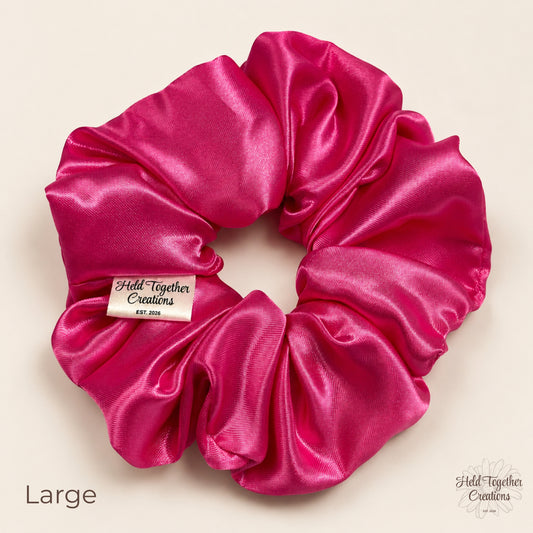 Large pink satin scrunchie laid flat showing glossy gathered fabric and HTC label.