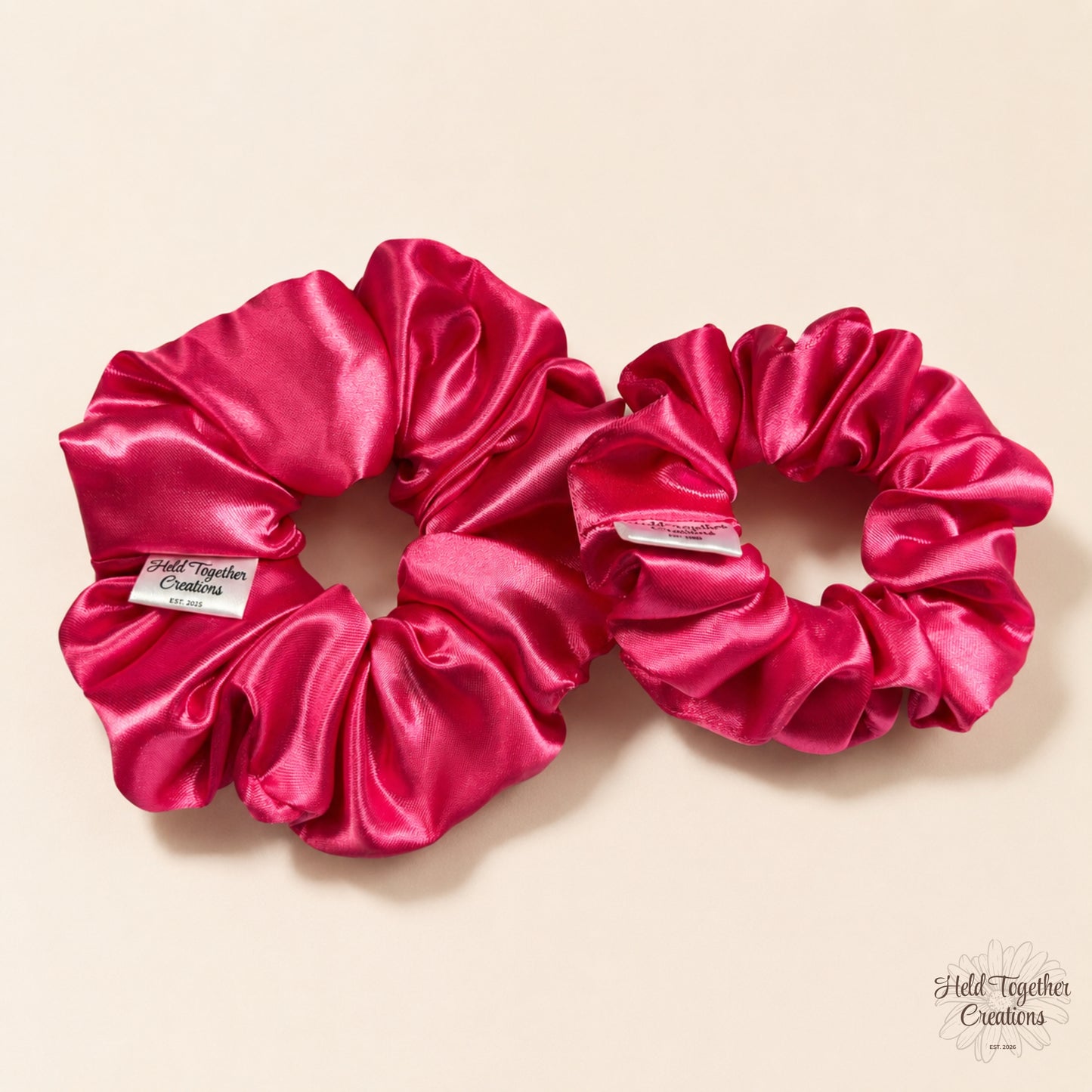 Small and large pink satin scrunchies side by side on a soft neutral background.