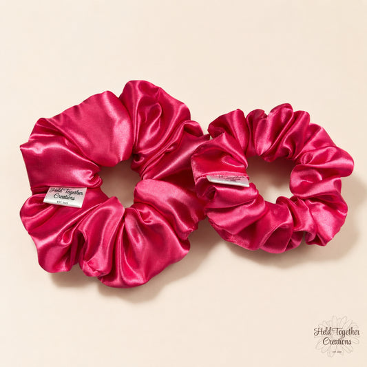 Small and large pink satin scrunchies side by side on a soft neutral background.